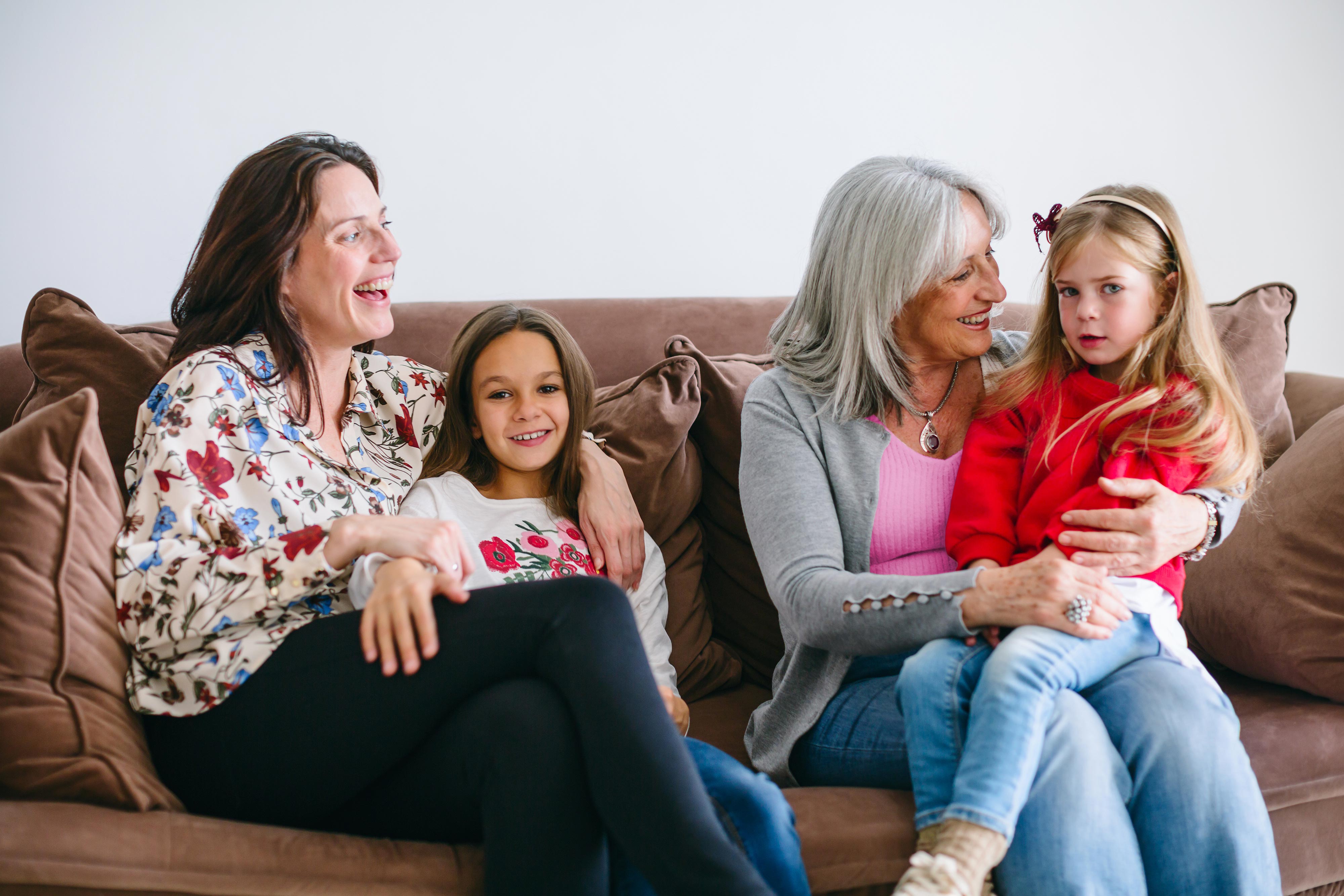 Three generations of women and children laughing on a sofa
