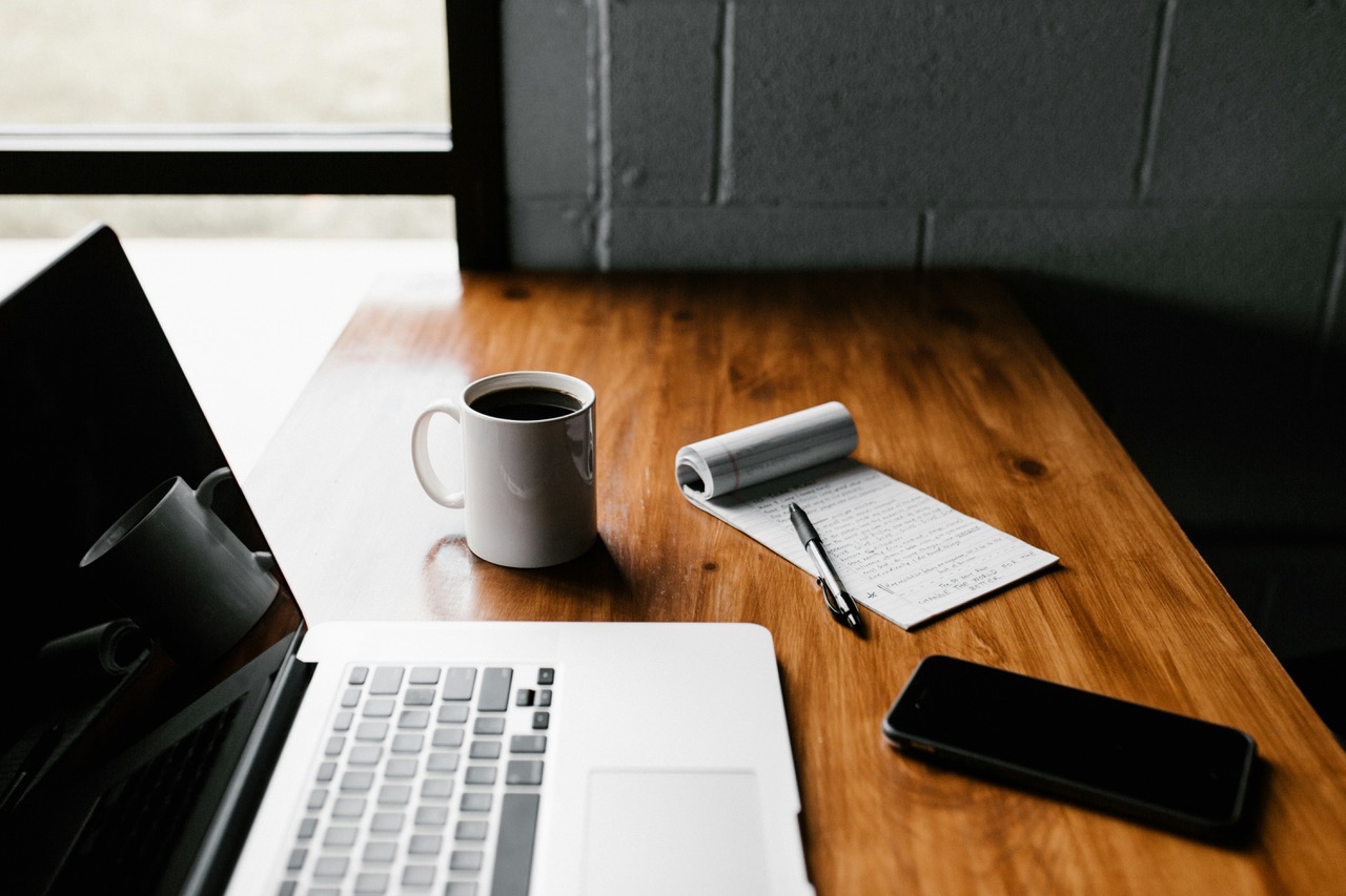 Desk with laptop, cup of coffee, phone and notepad