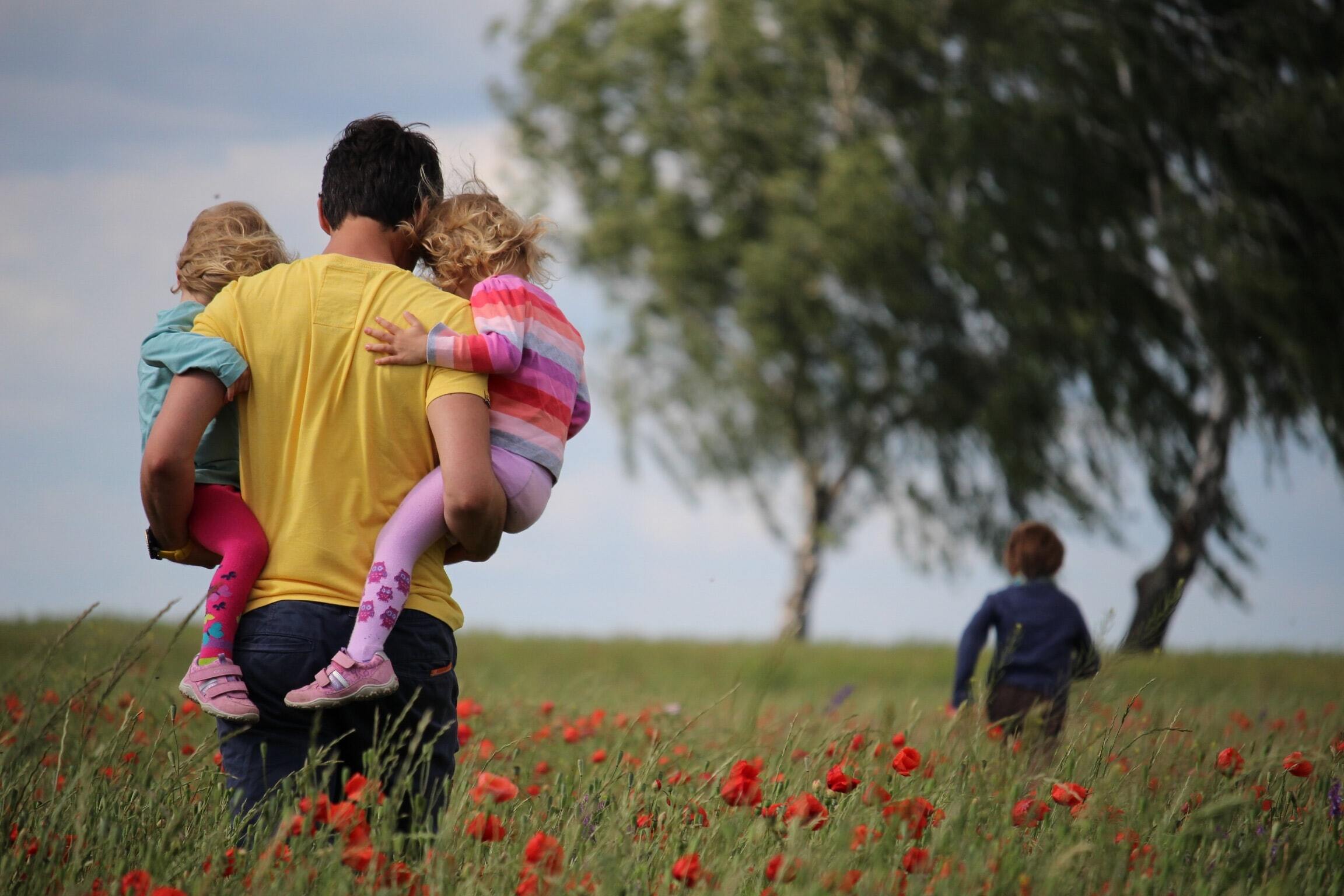 Dad carrying children across a field in the springtime.