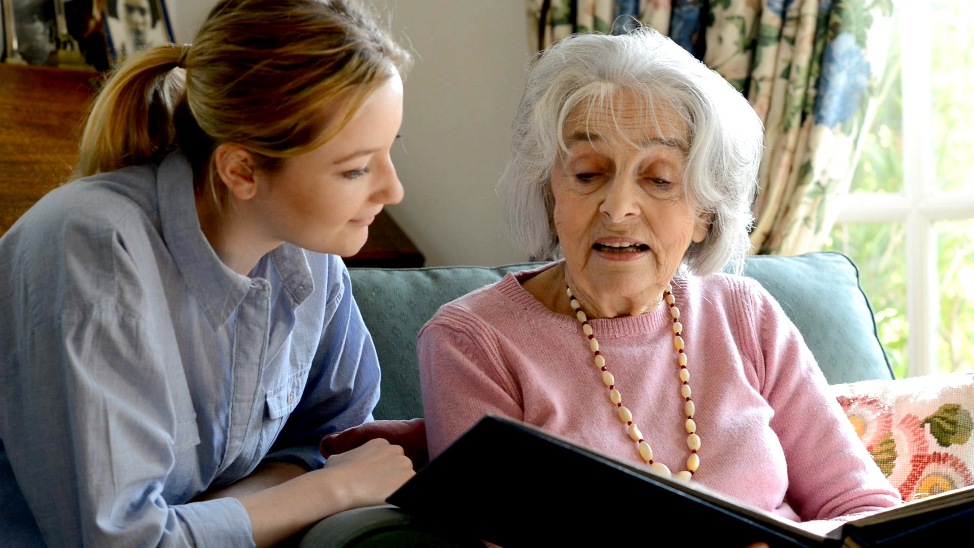 An elderly woman looking at a book with a younger woman