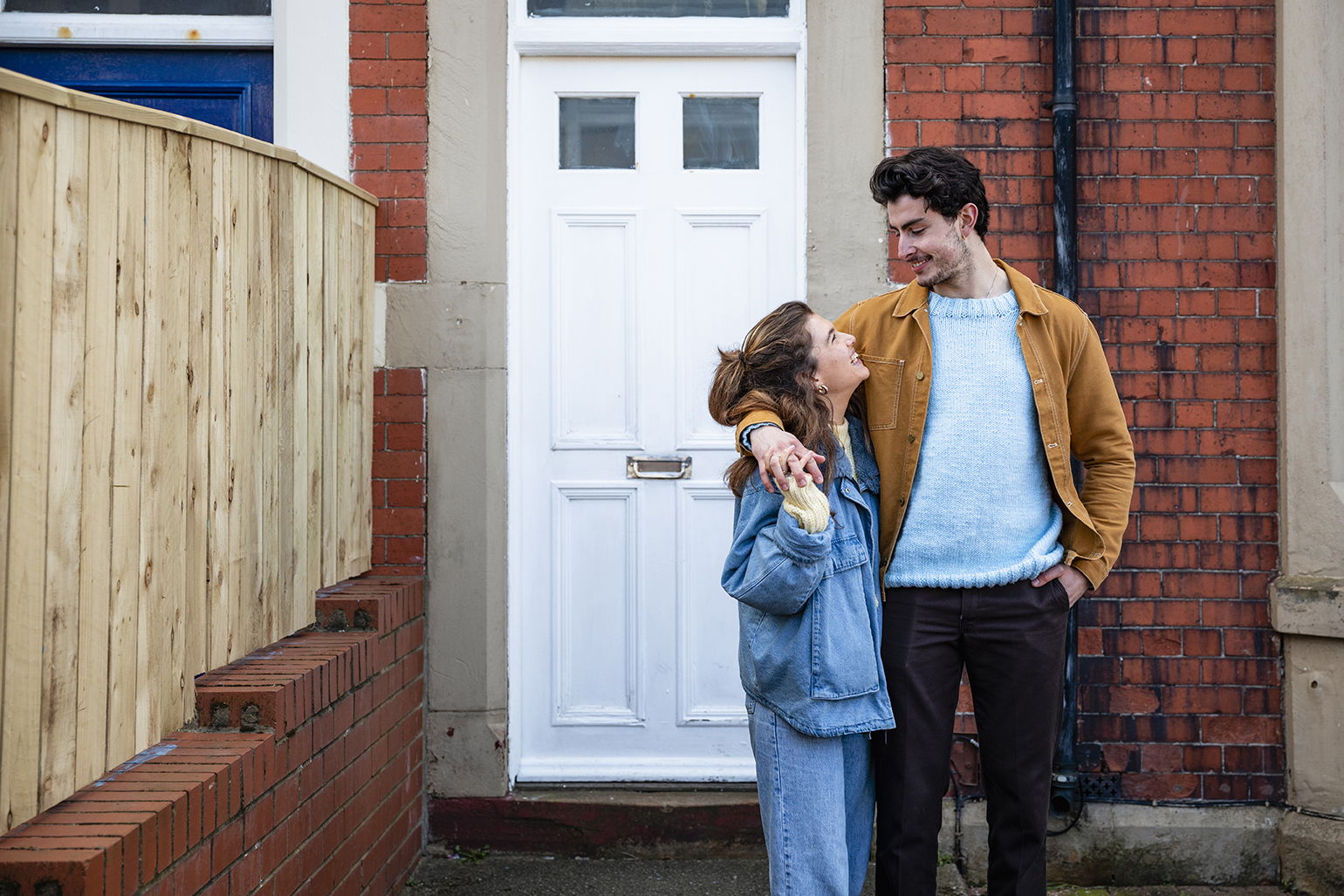 Steps to buying a house concept: young couple smiling outside their home.