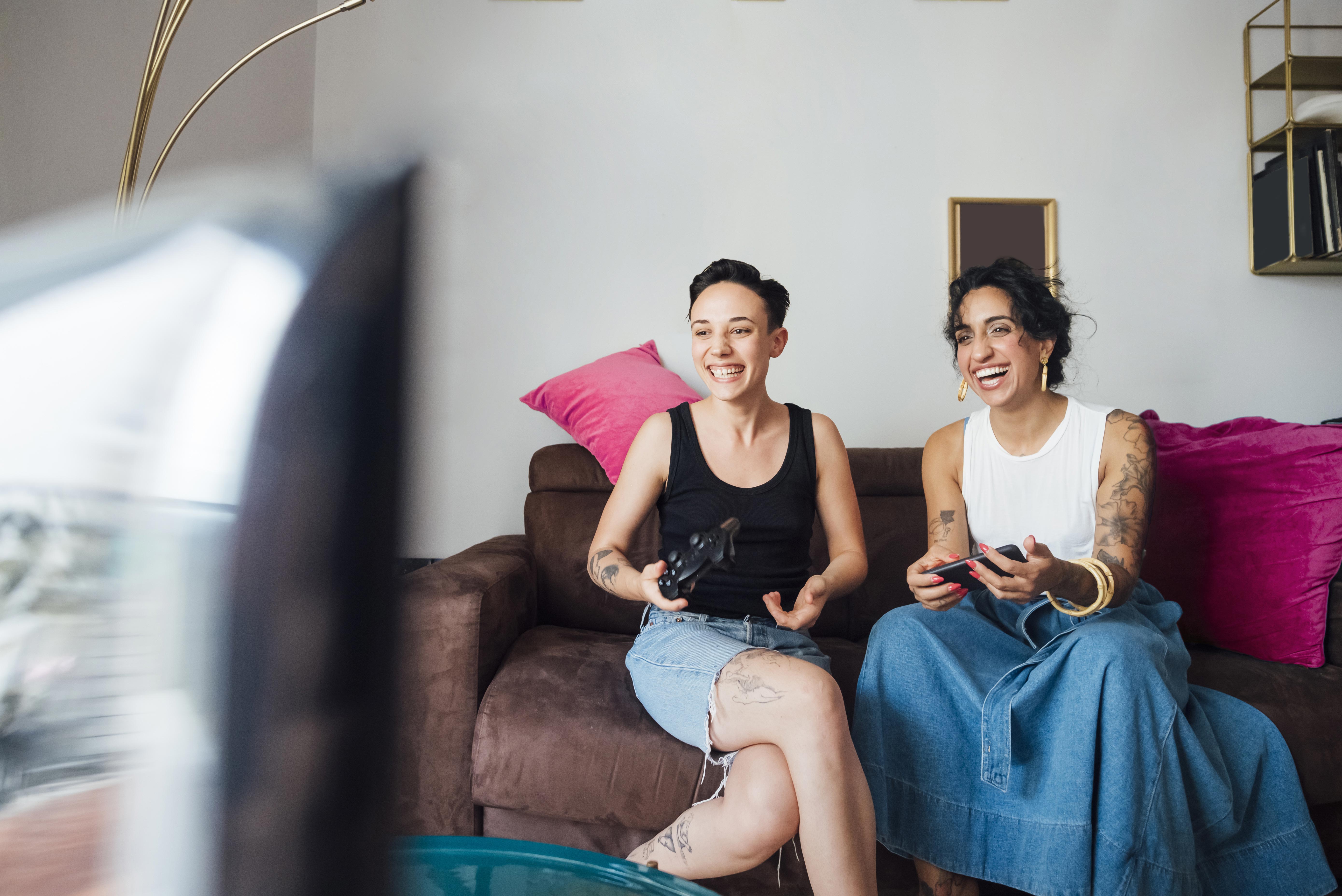 Two women sat on a sofa, smiling and enjoying their first home.