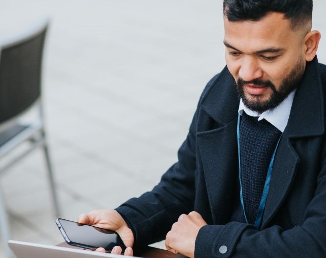 Man looking at a laptop holding a phone.