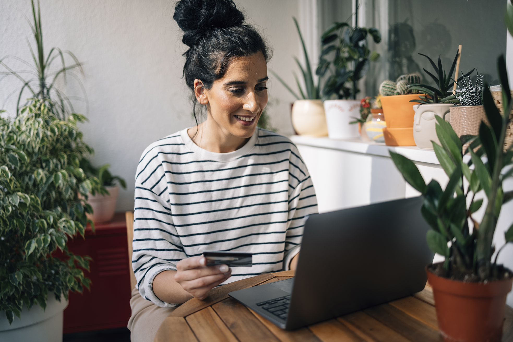 Easy access savings concept. Woman sat with laptop and holding bank card.